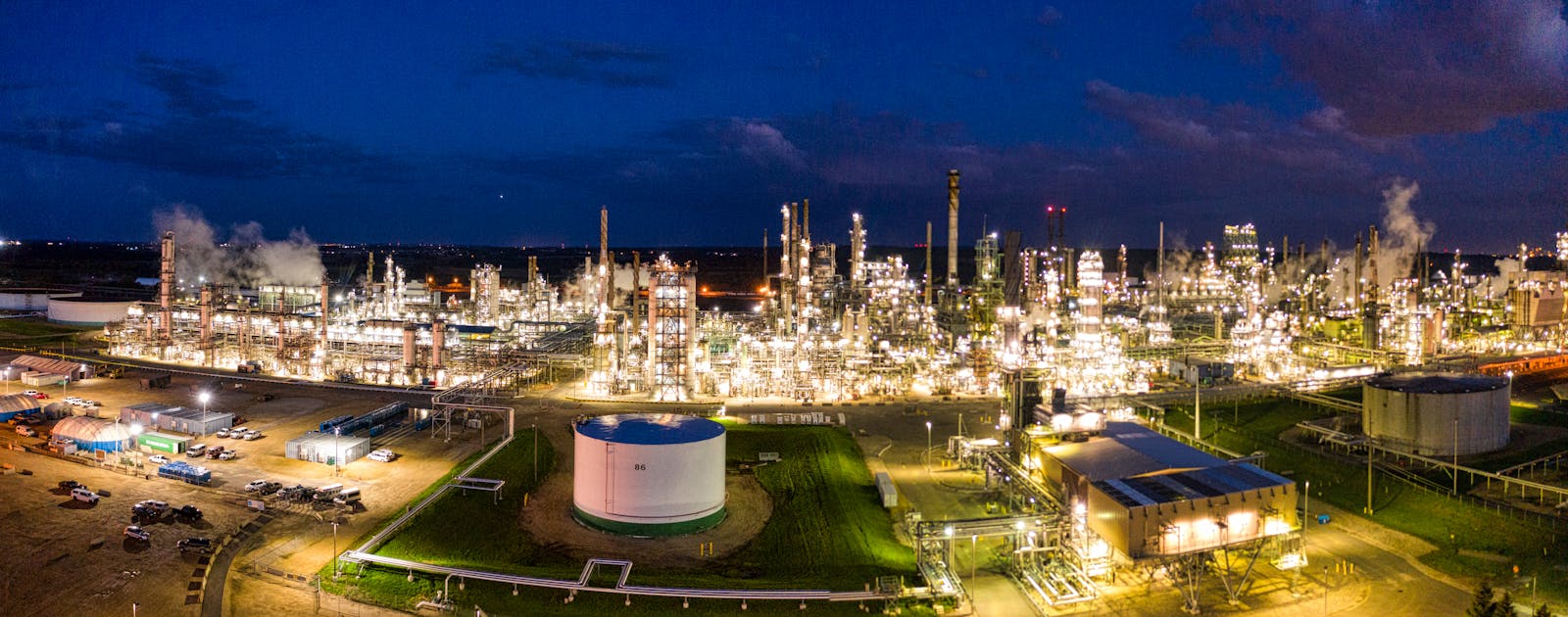 A brightly lit oil refinery at night with storage tanks and industrial towers